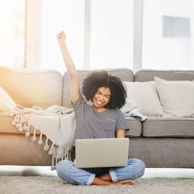 Shot of an attractive young woman using a laptop and cheering at home